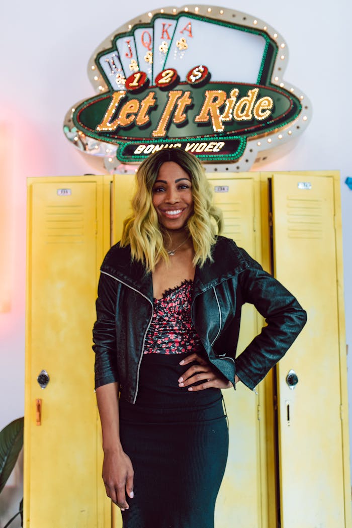 services-03 Stylish woman in a black leather jacket poses confidently in front of a retro casino sign indoors.